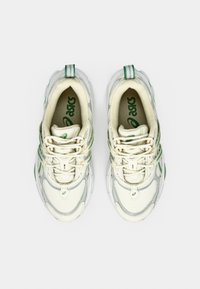 Světle béžové sportovní boty se zelenými akcenty. Síťovina a syntetické materiály. Zaoblená špička, ploché tkaničky a polstrované podrážky. Minimální značení.