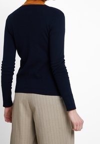 Mörkblå, figursydd tröja med långa ärmar och ribbad nederkant, tillsammans med ljusbeiga randiga byxor. Mjuk stickad textur, minimalistisk design.