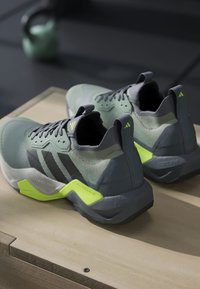 Baskets sportives avec une tige en mesh gris-vert, des accents gris et une semelle jaune vif. Présente un talon texturé et des détails de logo.