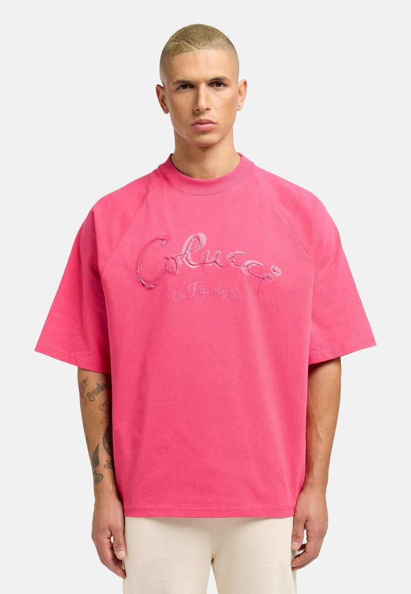 Lyserød bomulds oversized t-shirt med korte raglanærmer, prydet med broderet tekst "Colucci la Famiglia" på forsiden. Glat tekstur.