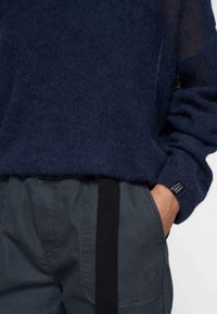 Granatowy sweter dziany o fakturowanym wykończeniu, zestawiony z szarymi spodniami z czarnym bocznym paskiem i logo w pobliżu kieszeni.