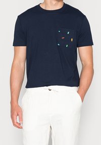 Marinblå bomullströja med korta ärmar och bröstficka som har färgglada broderade former i grön, gul och röd.