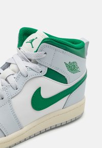 Szürke bőr magas szárú sneaker zöld kiegészítőkkel. Párnázott gallérral, fűzős elülső résszel és texturált gumitalppal rendelkezik. Az Air Jordan logó látható.