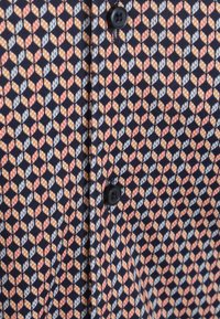 Geknoopte shirt met een marineblauwe achtergrond en een geometrisch patroon in oranje, wit en grijs. Textuurstof met een dicht geweven ontwerp.