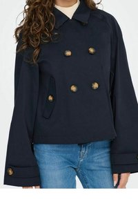 Chaqueta azul marino de doble botonadura, hecha de un tejido resistente, con grandes botones dorados, mangas anchas y bolsillos laterales.