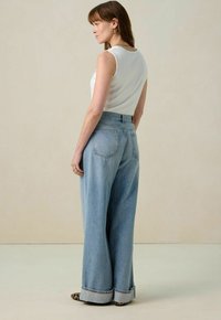 Hoge taille, wijdvallende blauwe jeans van denim met een lichte wassing. Voorzien van opgerolde manchetten en twee achterzakken. Model draagt een witte aansluitende top.
