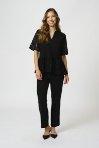 Top in pizzo nero con maniche corte e design peplum, abbinato a pantaloni neri su misura e décolleté a punta.