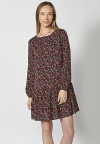 Schwarzes Kleid mit einem floralen Muster in Rot und Weiß. Lange Ärmel, runder Halsausschnitt und gestufter Rockdesign. Leichter Stoff.