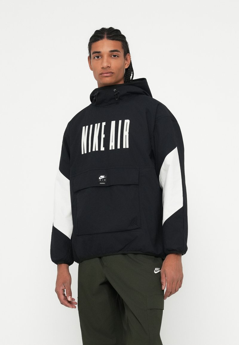 Juodas Nike Air pūkinis džemperis su dideliu baltu logotipu, baltais akcentiniais rankovėmis, priekinėmis kišenėmis ir reguliuojamu gobtuvu. Tekstūra lygi, medžiaga lengva.