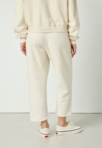 Krémovo sfarbené fleecové tepláky s voľným strihom, skrátenou dĺžkou a rebrovanými manžetami, kombinované s bielymi teniskami s červenými detailmi.