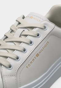 Λευκό παπούτσι Tommy Hilfiger με μπεζ κορδόνια, χρυσό λογότυπο στο πλάι και λεπτομερείς ραφές σε λείο δερμάτινο επάνω μέρος.