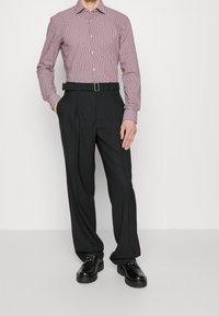 Punavalkopilkullinen pitkähihainen kauluksellinen paita, yhdistetty mustiin laskostettuihin housuihin ja mustiin nyörikenkiin. Vyö metallisoljella.