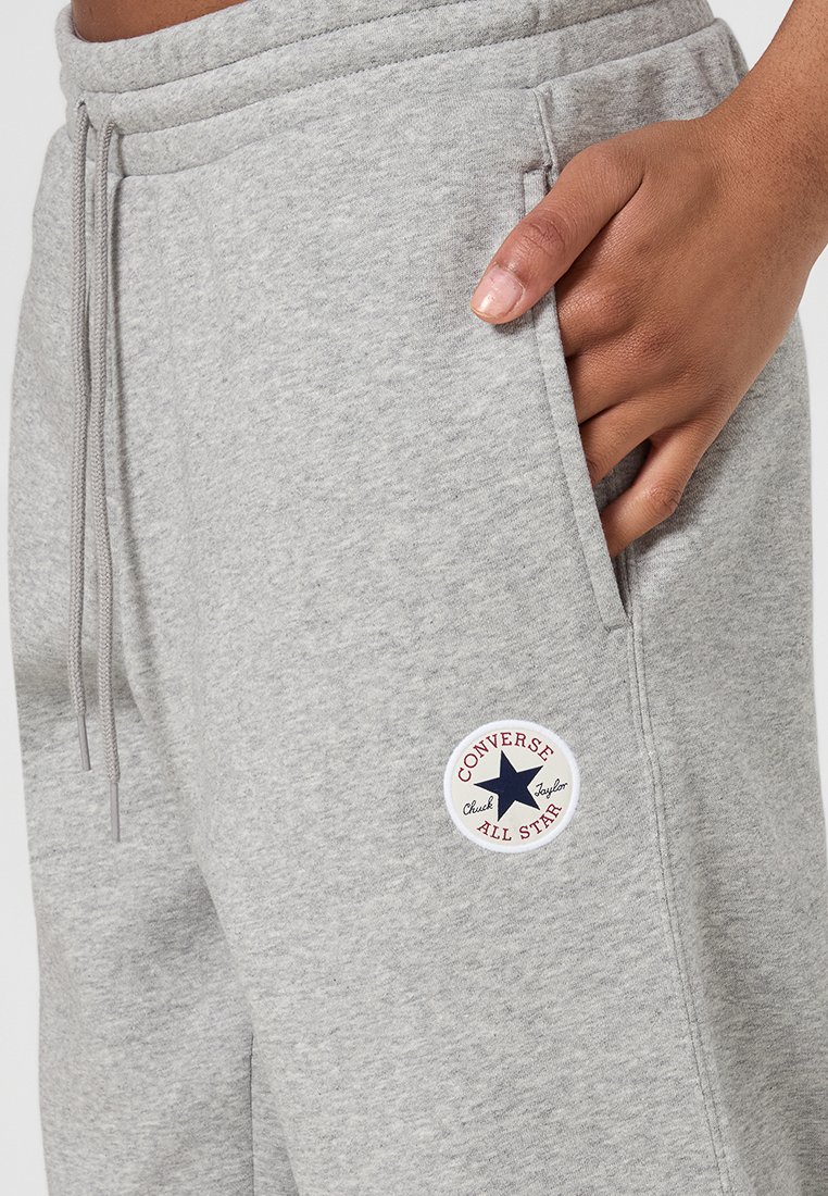 Szare dresy wykonane z miękkiego materiału posiadają elastyczny pasek w talii oraz boczne kieszenie, z okrągłą naszywką z logo Converse na udzie.