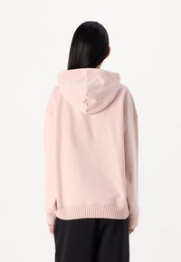 Felpa rosa con una texture morbida, design oversize, maniche ampie e orlo a coste. Presenta un cappuccio con cordino e fessure laterali.