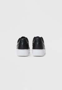 Crne kožne tenisice s teksturiranim leđima, bijelim gumenim potplatima i crnim mrežastim detaljima. Imaju utisnuti brend na peti.