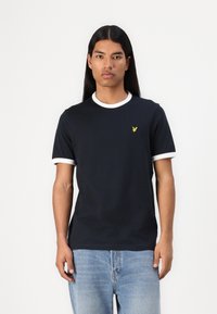 T-shirt bleu marine avec col et poignets côtelés blancs, présentant un petit logo jaune sur la poitrine gauche. Coupe slim et texture douce.