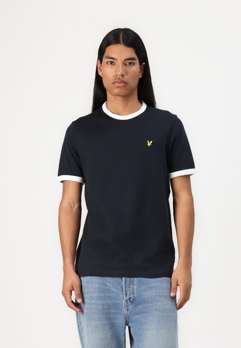 T-shirt bleu marine avec col et poignets côtelés blancs, présentant un petit logo jaune sur la poitrine gauche. Coupe slim et texture douce.