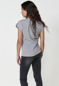 Grå kortärmad t-shirt med avslappnad passform och mjuk textur, som kombineras med mörkgrå slim-fit jeans med sidodetaljer och fickdetaljer.