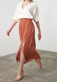 Gonna a pois color ruggine con uno spacco, abbinata a una maglietta bianca a scollo a V con maniche a sbuffo. Il modello indossa scarpe con tacco beige.