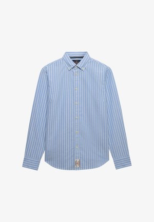 Lyseblå langærmet skjorte med knapper og hvide lodrette striber samt knappet krave, med et lille brandlabel nær nederste kant.