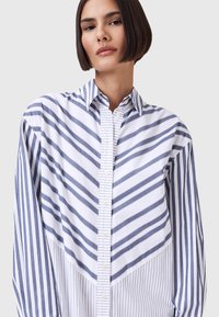 Witte knopshirt met blauwe diagonale en verticale strepen. Bevat een puntige kraag en heeft een ontspannen pasvorm met een gestructureerde stof.