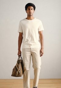 Μπεζ κοντομάνικη μπλούζα, κρεμ παντελόνια με ριμπ ύφασμα και καφέ δερμάτινη τσάντα duffel. Μινιμαλιστικός σχεδιασμός με άνετη εφαρμογή και λεία υφή.