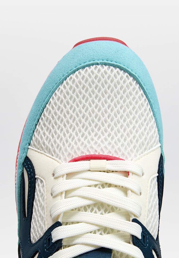 Siatkowe sneakersy z białą cholewką, akcentami z turkusowego zamszu, czerwonymi detalami i białymi sznurówkami. Posiadają teksturowaną podeszwę dla lepszej przyczepności.