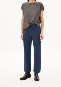 T-shirt à manches courtes rayé gris associé à un pantalon large marine, complété par des bottines noires, sur fond blanc.