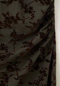 Motif floral en velours marron foncé sur tissu vert foncé texturé avec des plis doux et un drapé.