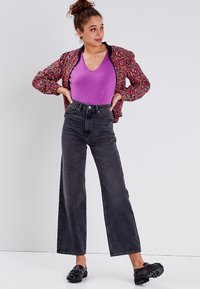 Giacca bomber floreale, top viola a scollo a V, jeans neri a gamba larga con vita alta e mocassini neri con dettagli decorativi.