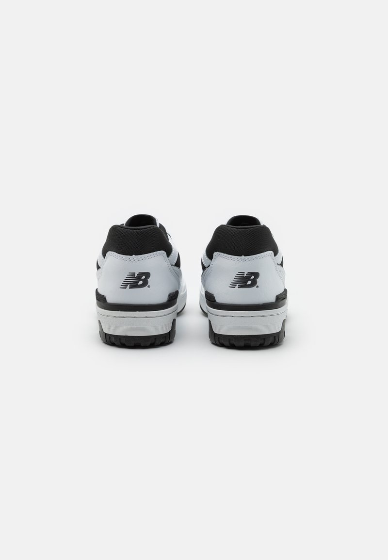 Zapatillas atléticas en blanco y negro con un diseño elegante, que cuentan con una suela texturizada, refuerzo en el talón y una marca visible en la parte posterior.