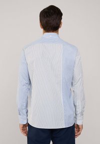 Camisa blanca con rayas verticales azules, de mangas largas, con puños abotonados y detalles en la sisa trasera. Tejido de algodón suave con un corte ajustado.
