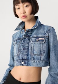 Kratka traper jakna u svijetloplavoj boji s izblijeđenom teksturom, s metalnim dugmadima, dva prednja džepa i oznakom Calvin Klein na lijevoj strani.