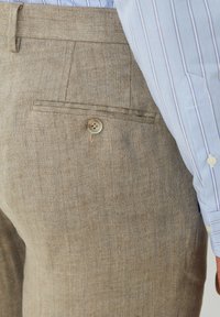 Pantaloni in lino di un colore marrone chiaro con una finitura testurizzata, dotati di una tasca posteriore e di una chiusura a un bottone per i dettagli.