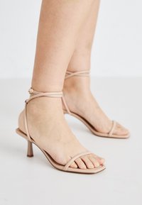 Sandales nues à brides avec une fine bride de cheville, un design à bout carré et un petit talon carré. Texture lisse avec un minimum de détails.