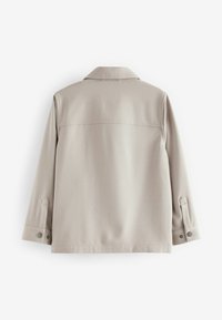 Beige långärmad jacka med krage, som har en ryggsöm, knäppta ärmslut och en slät, strukturerad tyg.