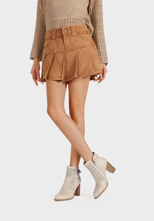 Gonna di jeans a pieghe marrone con passanti per cintura, abbinata a stivaletti crema alla caviglia con accenti perforati e tacco impilato.