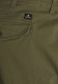 Olivově zelené kalhoty se jemnou texturou, s malou černou nálepkou "JACK & JONES" poblíž kapsy a jemnými švy.