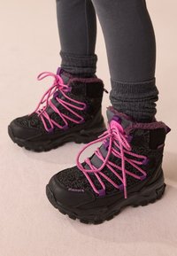 Schwarze Wanderschuhe mit filigranen Blumenmustern, lila Akzenten und pinken Schnürsenkeln. Mit Fleecefutter am Kragen und robusten Sohlen für guten Halt.
