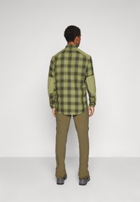 Chemise à carreaux verte avec des manches vertes contrastantes, associée à un pantalon cargo olive. Fabriquée en tissu durable et offrant une coupe décontractée.