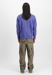Lilla crewneck sweatshirt parret med olivengrønne cargo-bukser med flere sidelommer og en afslappet pasform. Enkle teksturer, neutral baggrund.