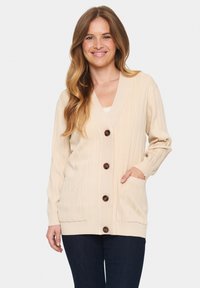 Bežinė švelni medvilninė megztinis su raukšlėmis, turinti V formos iškirpę, mygtukų užsegimą, dvi kišenes ir ilgas rankoves.