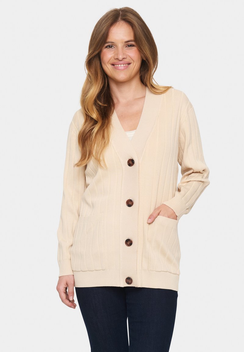 Bežinė švelni medvilninė megztinis su raukšlėmis, turinti V formos iškirpę, mygtukų užsegimą, dvi kišenes ir ilgas rankoves.