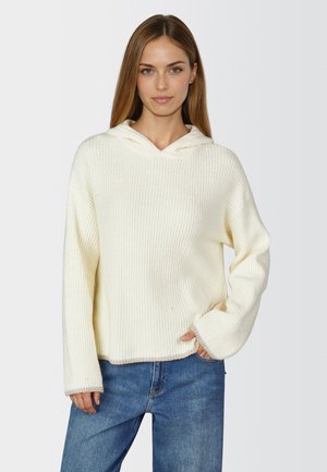 Weißer, gerippter Strickhoodie mit lässiger Passform, der über einen Kordelzug, lange Ärmel und kontrastierende Saumdetails verfügt. Kombiniert mit blauer Jeans.