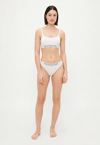 Bralette de algodão branco e cuecas de bikini combinando com um design ajustado, apresentando uma faixa preta com logótipo ao redor da cintura e do busto.