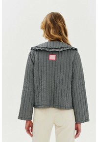 Prošívaná černobílá károvaná bunda s volánkovým límcem a růžovou nášivkou na zadní straně. Dlouhé rukávy s volným střihem.