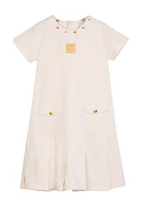 Abito color crema con maniche corte, borchie dorate attorno al collo, patch con logo centrato e due tasche anteriori con bottoni dorati.