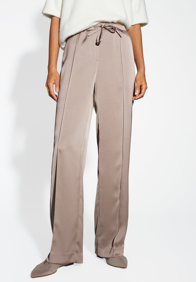 Beige wijde broek met een drawstring taille, zachte stof en voornaden, met een gladde, vloeiende textuur en een eenvoudige uitstraling.