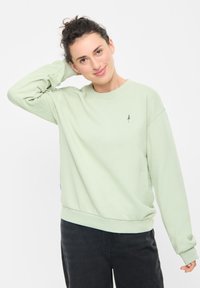 Felpa verde chiaro con scollatura rotonda e polsini a costine, caratterizzata da un piccolo logo ad albero sul petto e una vestibilità comoda.