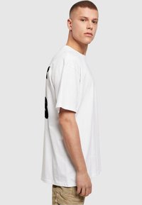 Hvid bomulds t-shirt med korte ærmer, der har et stort sort grafik på siden. Enkel design med en afslappet pasform.